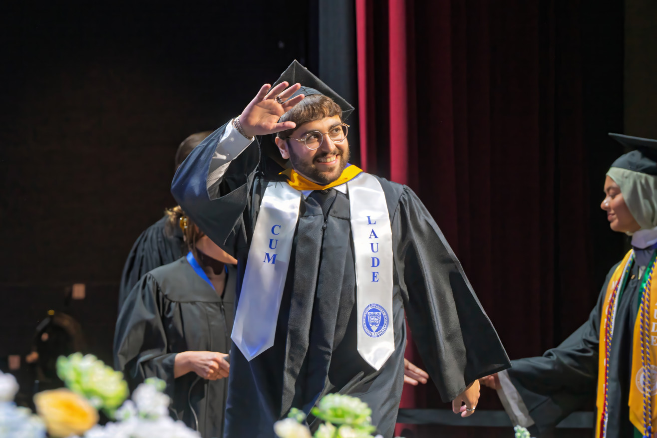 a young man waves before receiving his degree 