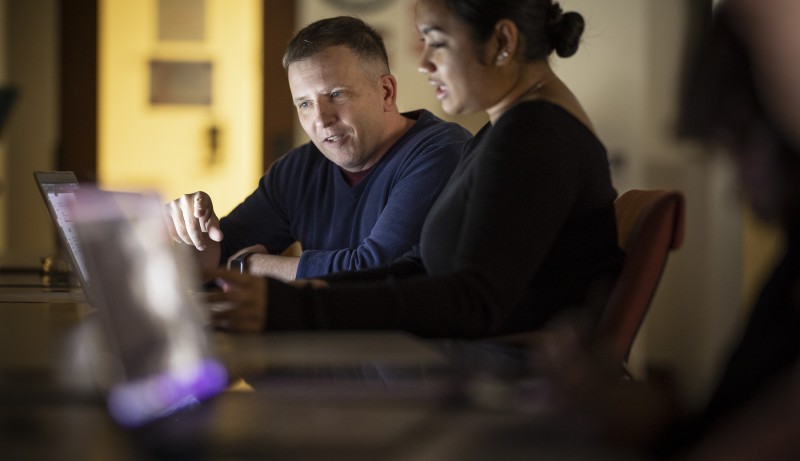 A man and a woman sitting next to each other having a discussion in front of a laptop